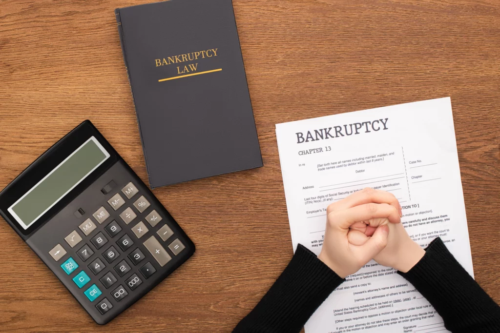 Person sitting at a desk with bankruptcy law book, calculator, and Chapter 13 paperwork, representing financial decision-making before filing bankruptcy.