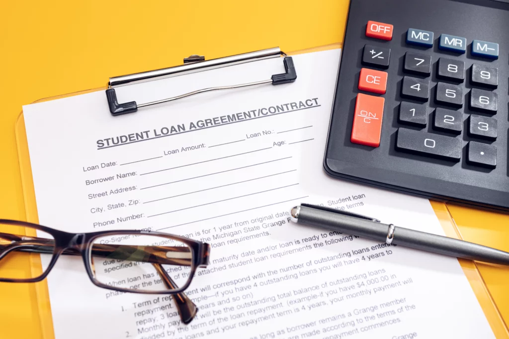 Student loan agreement form with calculator, glasses, and pen on desk, representing financial stress and bankruptcy options for student debt.